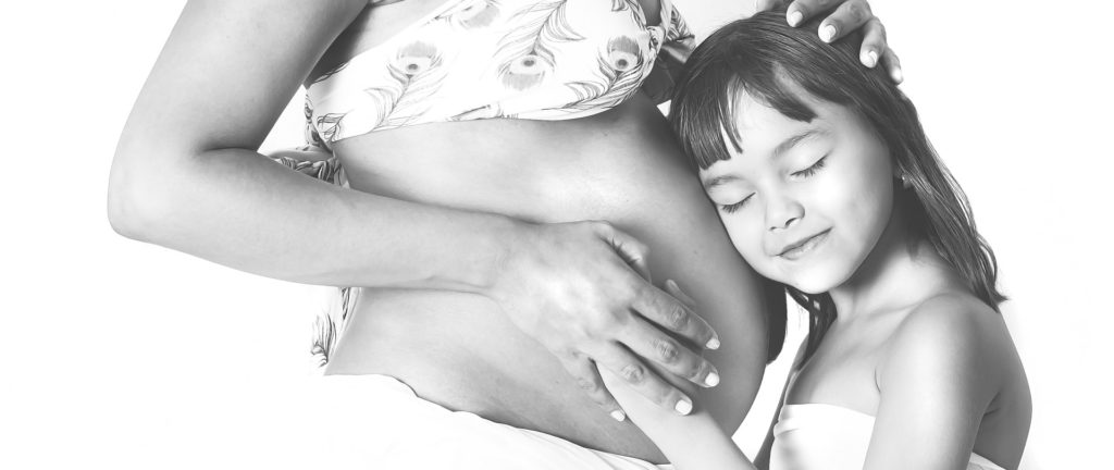 Na zdięciu dziewczynka przytla się do dużego brzucha mamy, w tej sytuacji możemy sprawić ulgę kobiecie w ciąży poprzez wykorzystanie terapii, którą stanowi masaż leczniczy katowice